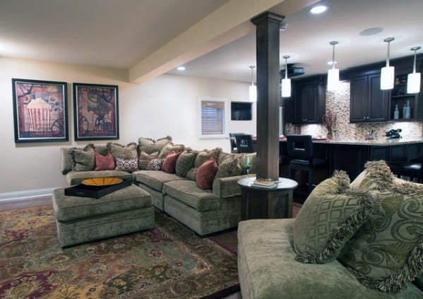 Basement with green sectional sofa, decorative rug, and open kitchen area with pendant lighting.