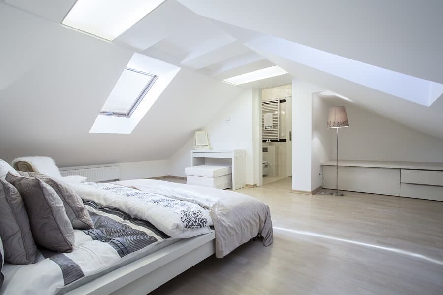 White, bright attic bedroom with a sloped ceiling, bed, dressing table, open door to bathroom, and modern decor