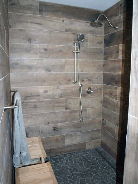 Shower with wood-look vinyl tiles, stone floor, and bench, featuring dual showerheads.