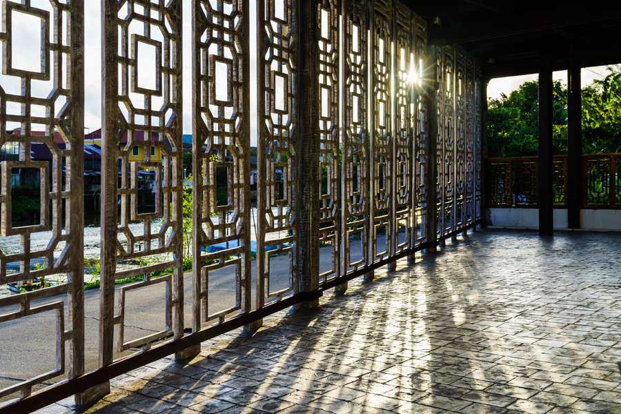 Carved wooden panel screen with intricate geometric patterns casting shadows on a tiled floor.