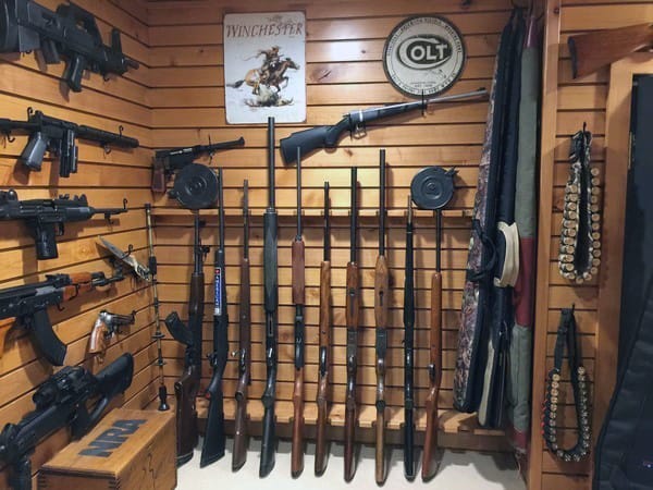 Wood-paneled gun room with rifles, shotguns, and vintage firearm-themed decor.