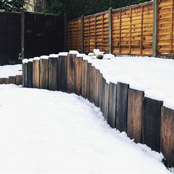 Wooden retaining wall in a snow-covered yard with wooden fencing in the background.