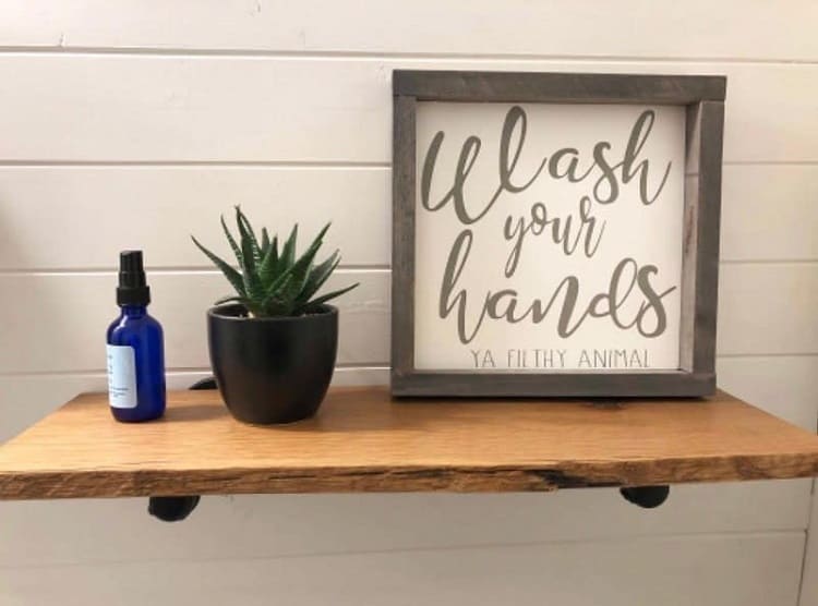 Wood bathroom shelf with "Wash Your Hands" sign, plant, and blue spray bottle.