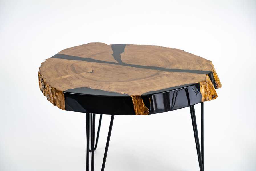 Round wood slab coffee table with black resin details and metal legs in a minimalist style.