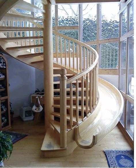 Curved wooden staircase with a slide beside large sunlit windows