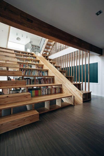 A wooden staircase with integrated bookshelves and a slide leads to a loft in a modern, open space
