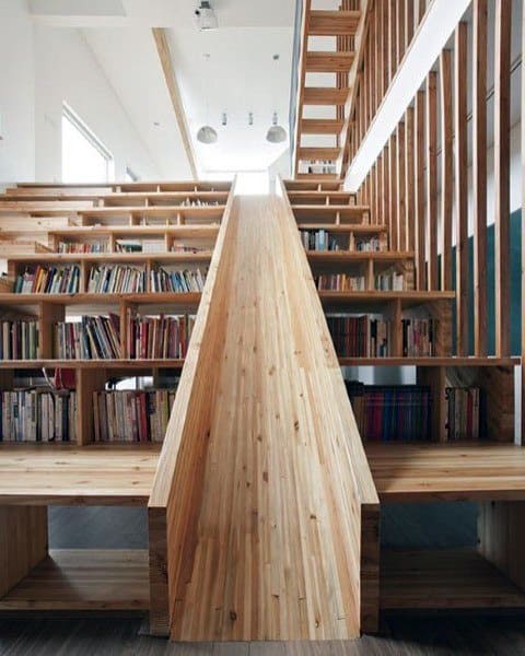 A wooden slide seamlessly integrated into a staircase and bookshelves, creating a modern library setting