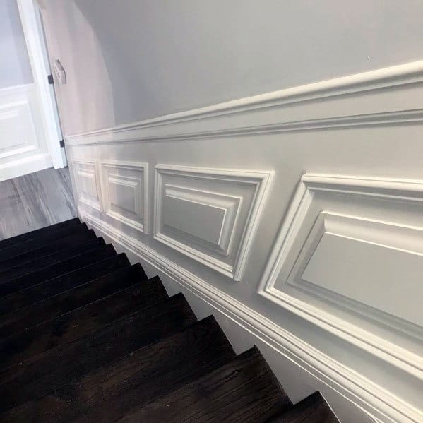 Stairway with dark steps and decorative white wainscoting and chair rail on walls
