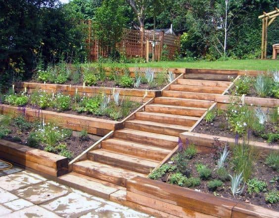 Terraced garden with wooden steps and lush plants, surrounded by trees and greenery