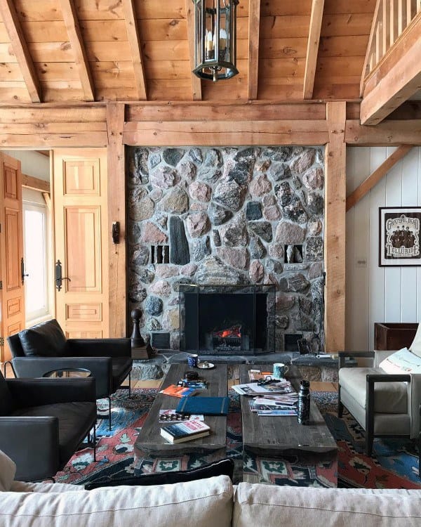 Cozy living room with a rustic stone fireplace framed by wooden beams under a warm vaulted ceiling.