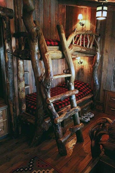 Rustic bunk beds with red plaid bedding in a cozy, log cabin-style room with warm lighting