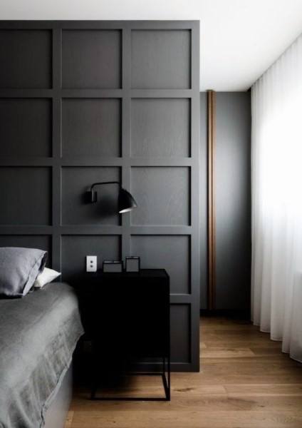 Modern black bedroom with paneled accent wall, minimalist nightstand, and soft sheer curtains.