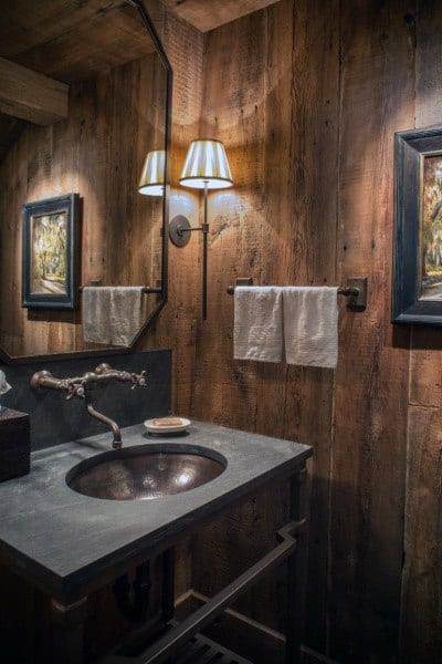 Rustic bathroom with wooden walls, metal sink, and cozy wall-mounted light