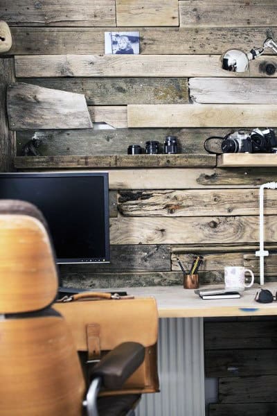 A rustic workspace with a wooden wall, cameras, a computer monitor, and a chair in the foreground