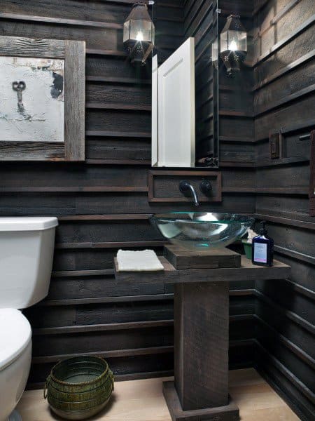 Rustic half bath with dark wood walls, a glass sink, artwork, and two lantern-style lights