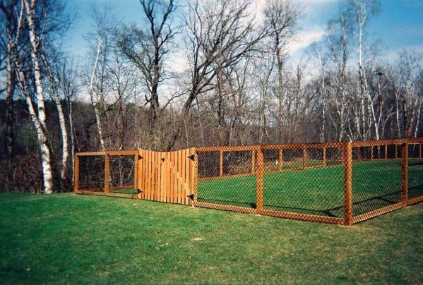 A fenced yard with a wooden gate, surrounded by trees and lush grass