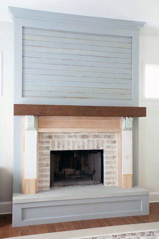 Brick fireplace with a distressed wood frame, dark wood mantel, and light blue shiplap paneling.
