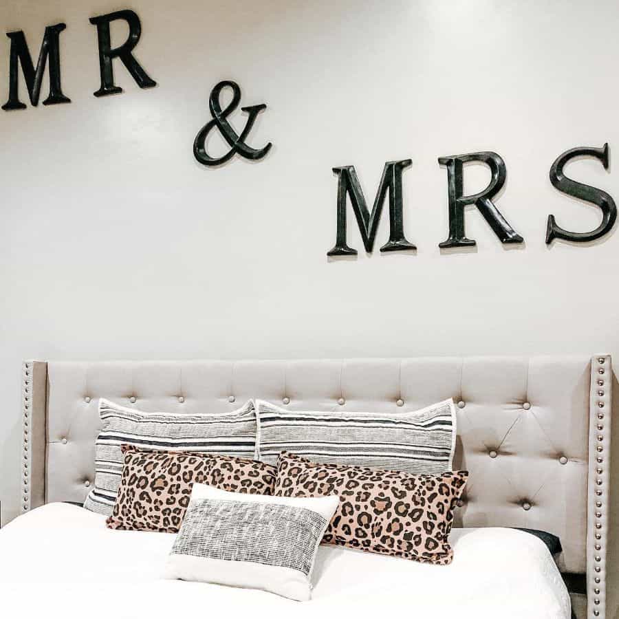 Modern bedroom with "Mr & Mrs" wall art, tufted headboard, and patterned accent pillows.