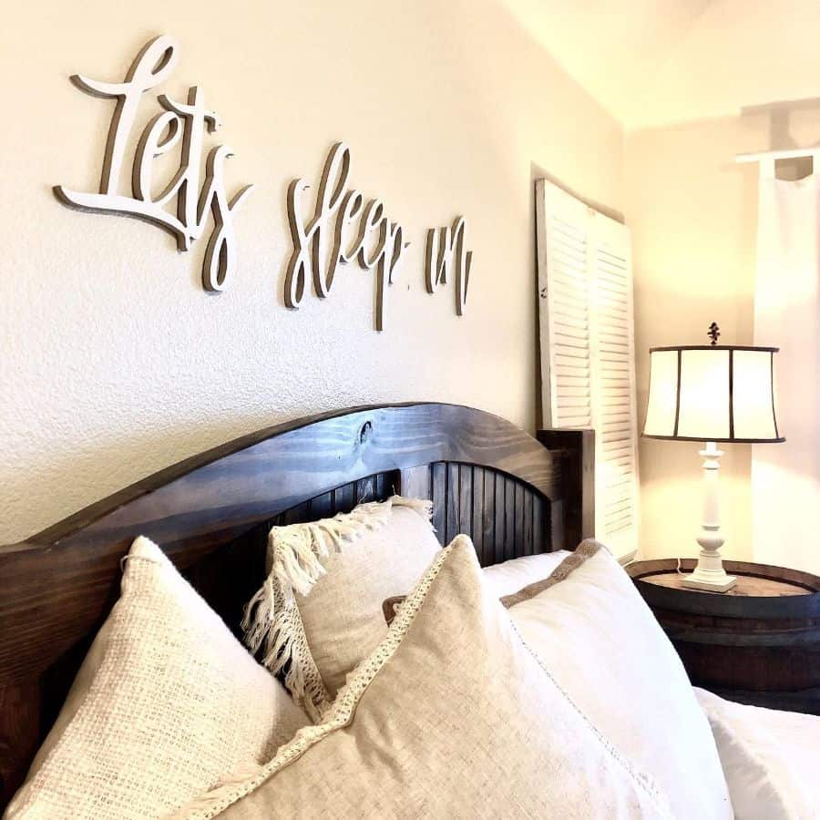 Rustic bedroom with "Let’s sleep in" wall art, wooden headboard, and cozy pillows.