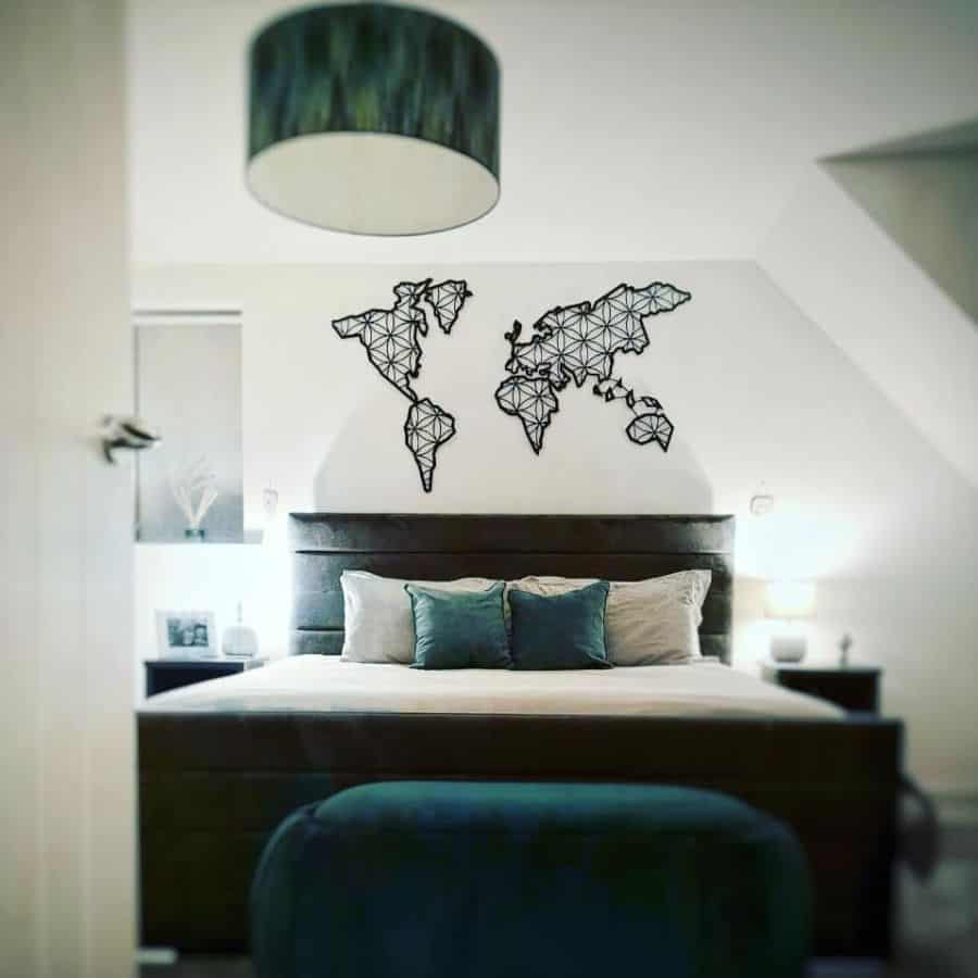 Modern bedroom with metal world map wall art and teal accent pillows.