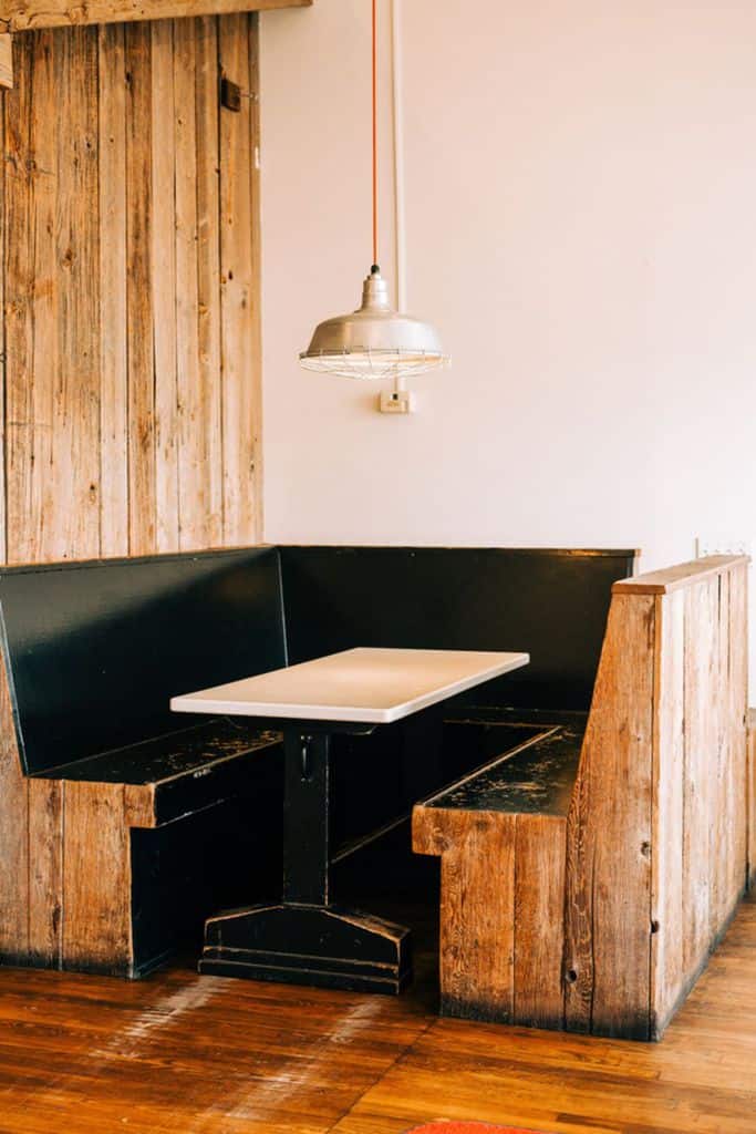 Rustic wooden booth seating with black benches and a simple pendant light fixture.
