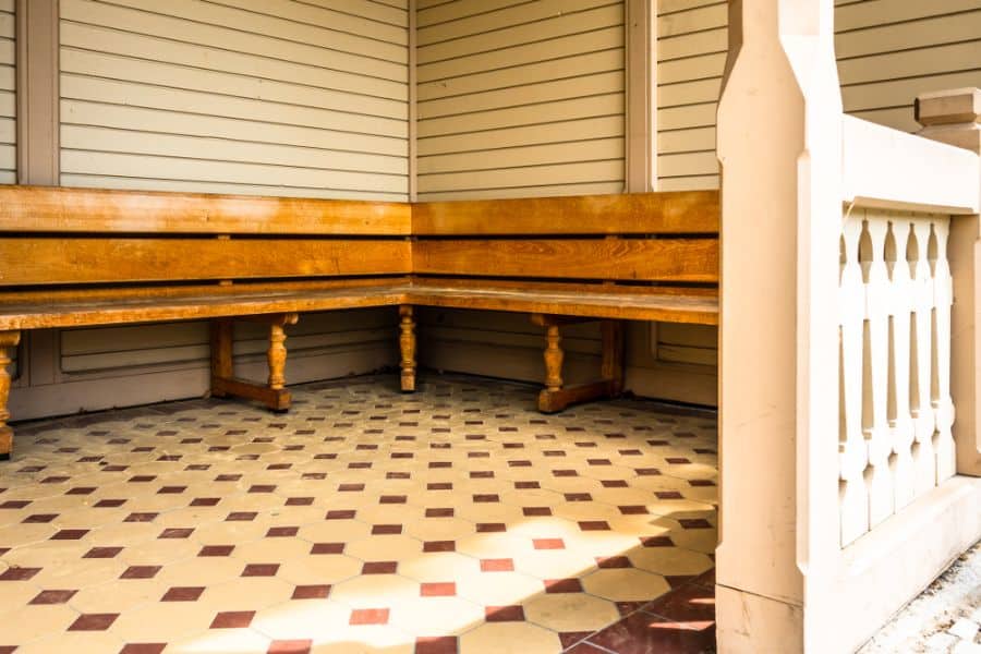 intage wooden bench seating on a tiled front porch with decorative railing.