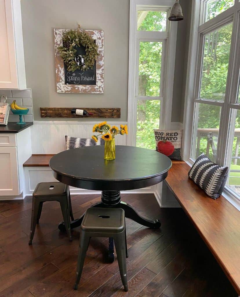 Cozy kitchen nook with a wooden banquette, black round table, and sunflower centerpiece.