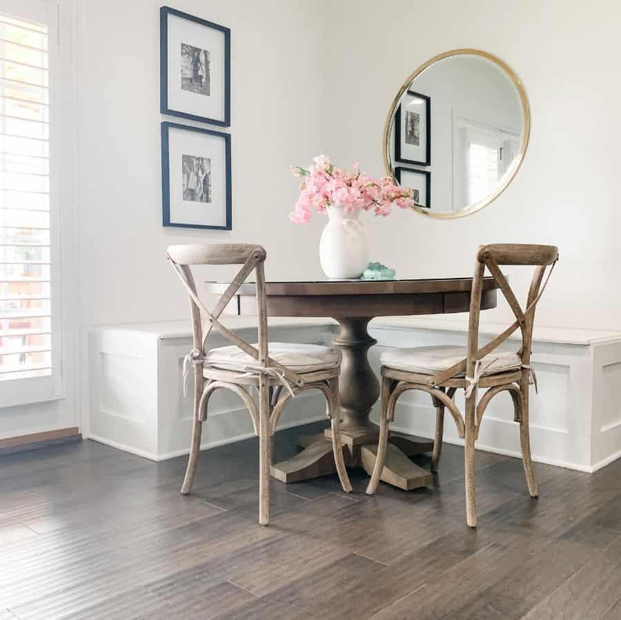 Charming dining nook with white banquette seating, wooden round table, and pink floral vase.