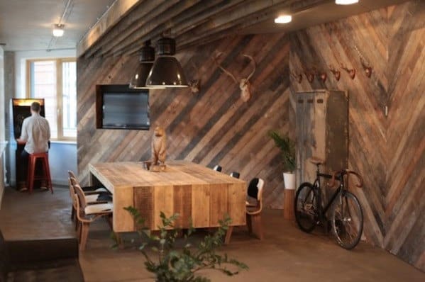 Cozy office with rustic wooden decor, a meeting table, bike, and a person playing an arcade game in the corner