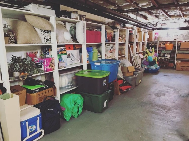 Basement storage with white wooden shelves holding bins, pillows, and various household items.