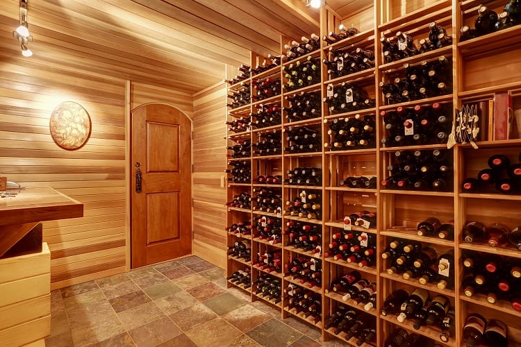 Spacious wine cellar with wooden racks and slate flooring, featuring a wooden door and warm lighting.