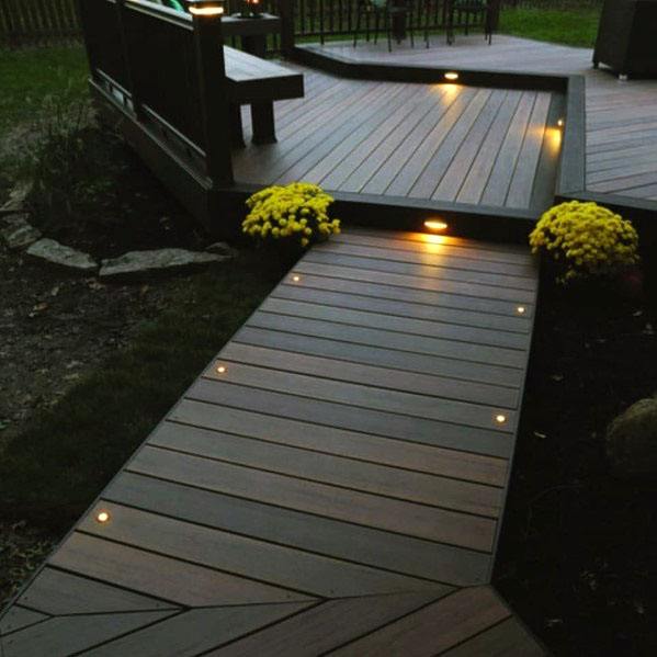 Walkway and deck with lights and potted yellow flowers on a dark evening