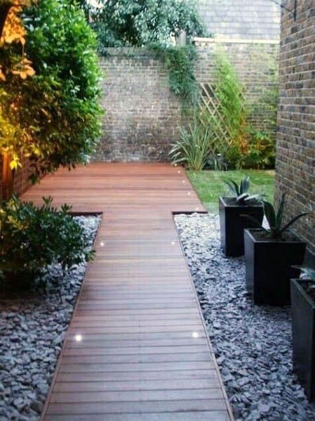 Walkway with wooden deck and lights, flanked by plants, stone, leading to a brick wall garden