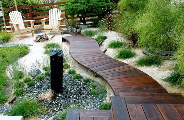 Walkway meanders through a landscaped garden with chairs and a fire pit