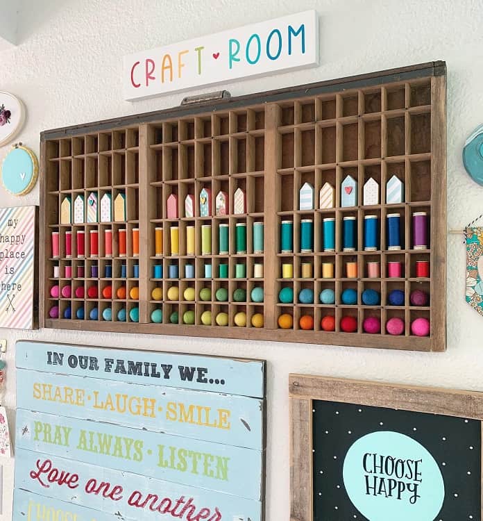 Craft room wall display with colorful wooden shelves holding various colored items and uplifting signs below