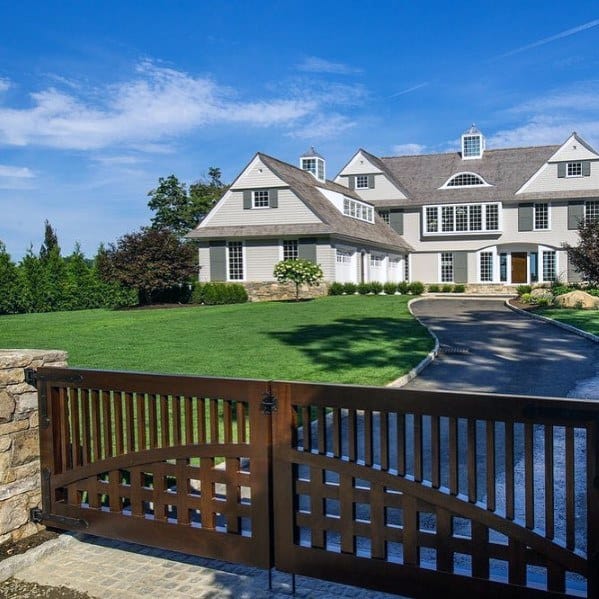 Wooden driveway gate with arched slat design and stone pillars.