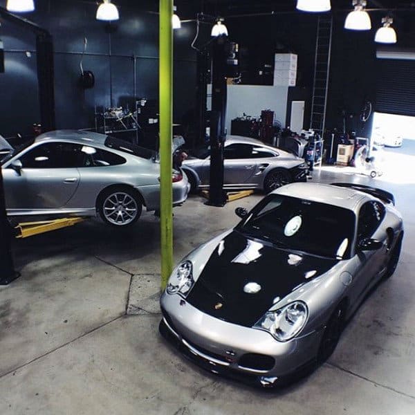 A sleek workshop-style dream garage featuring silver Porsches under bright industrial lighting.