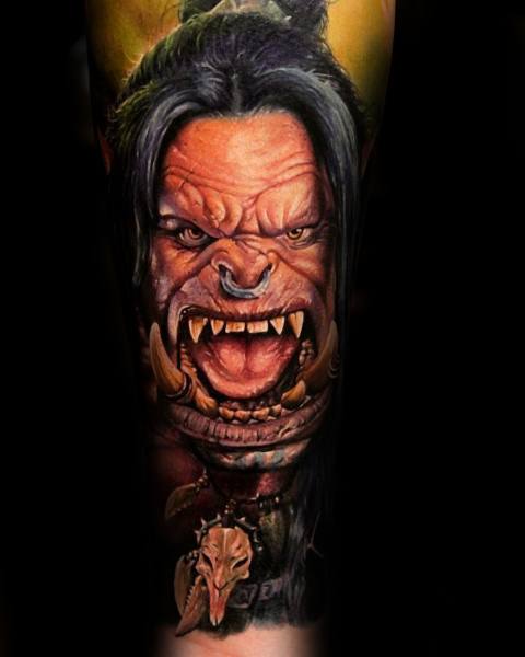 Hyper-realistic tattoo of a fierce orc from World of Warcraft, featuring sharp tusks, intense expression, and tribal accessories, inked with rich colors on the forearm.