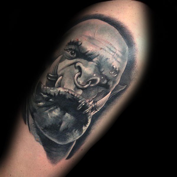 Realistic black and grey tattoo of an orc from World of Warcraft, featuring intense shading, fierce expression, and detailed tusks, inked on the upper arm.