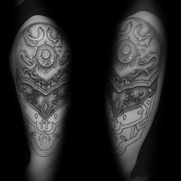 Black and grey tattoo of intricate World of Warcraft armor, featuring ornate patterns and a central emblem, inked on the upper arm.