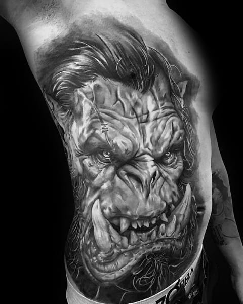 Realistic black and grey tattoo of a fierce orc from World of Warcraft, featuring intense details, scars, and sharp tusks, inked across the ribs and side.