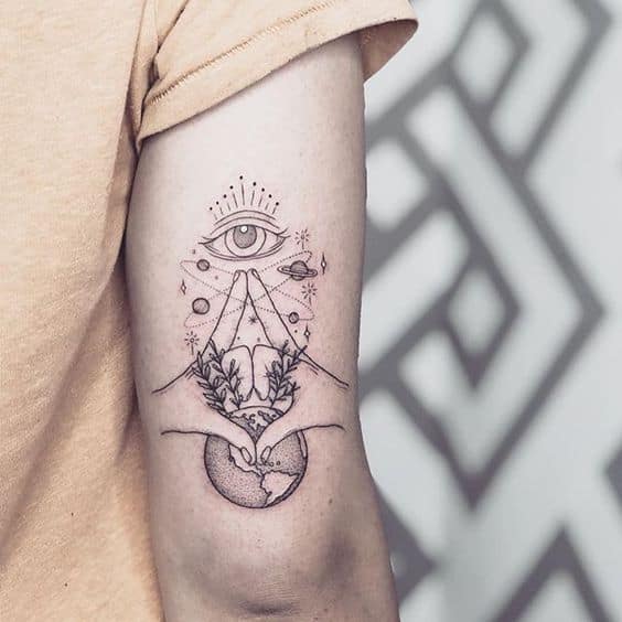 Minimalist tattoo of an all-seeing eye above mountains, planets, and hands holding the Earth, inked in fine black lines on the upper arm.