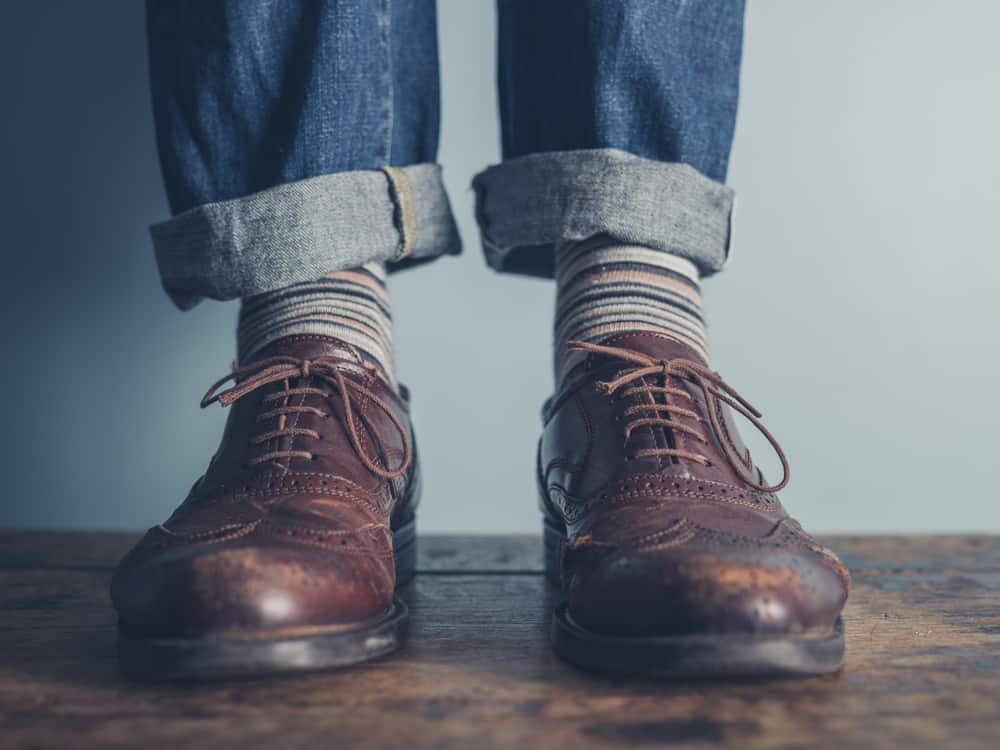 The feet of someone wearing a worn-in pair of brogues and cuffed jeans