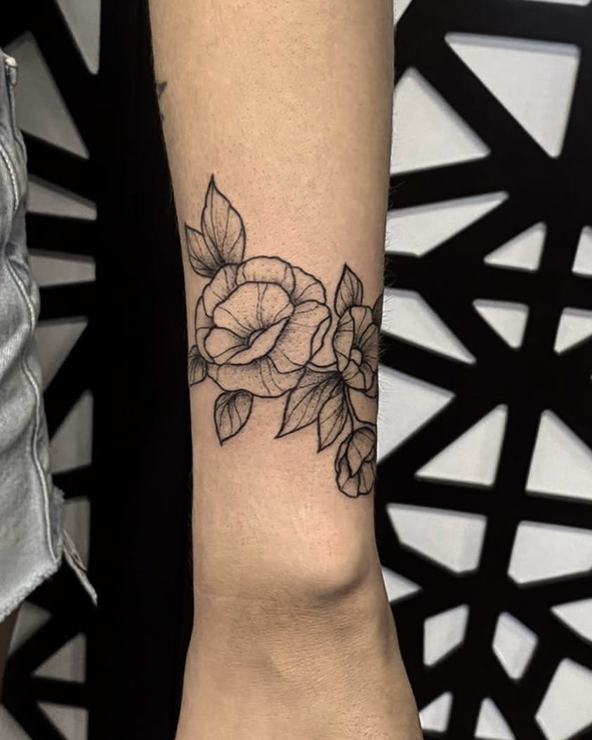Elegant black ink floral tattoo featuring two blooming roses and leaves, wrapping around the forearm