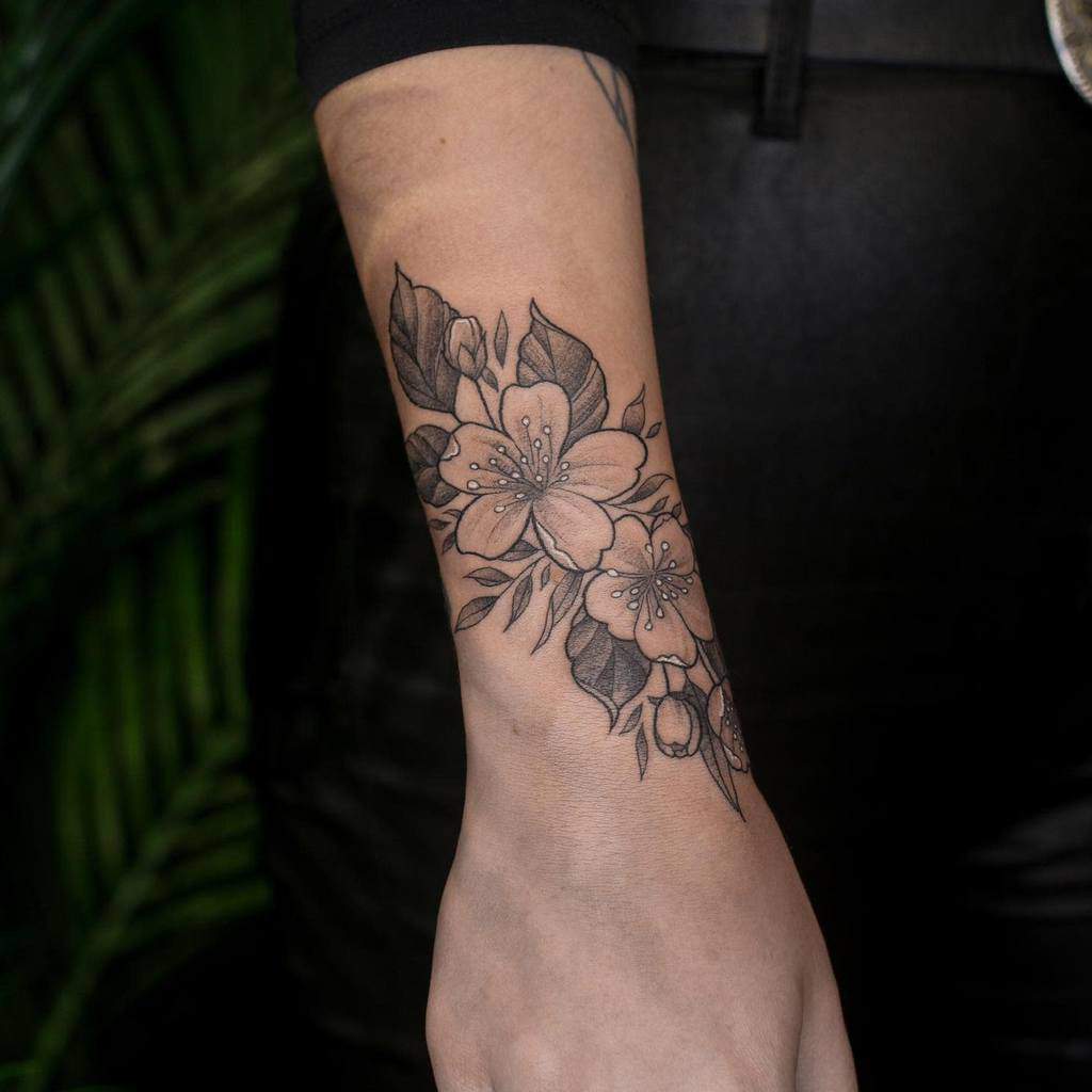 A stunning arm tattoo featuring detailed black and gray flowers and leaves gracefully extends to the wrist