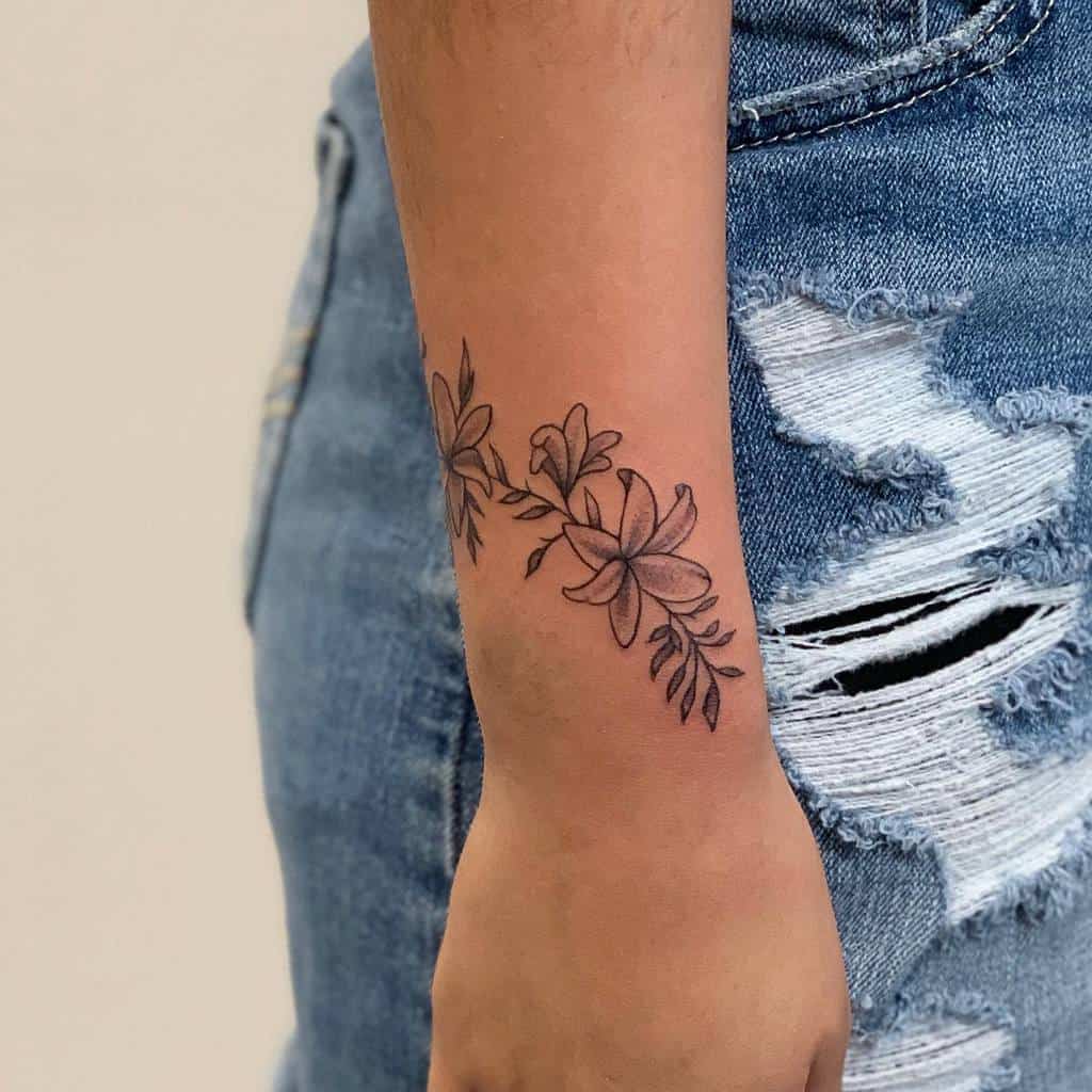 Delicate black ink floral tattoo with small flowers and leaves, wrapping around the wrist