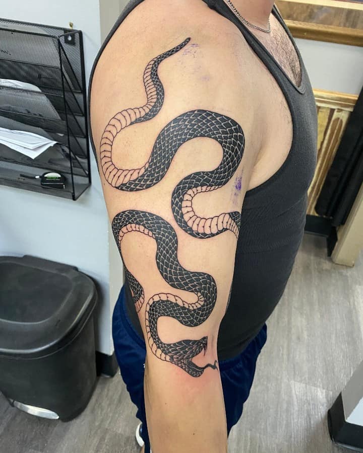 Bold black ink tattoo of a snake coiling around the upper arm, with intricate scale detailing and smooth shading