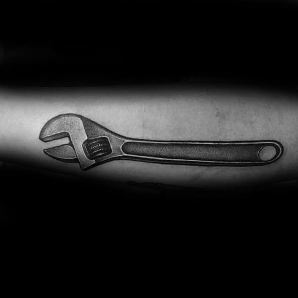 Realistic black and grey tattoo of an adjustable wrench on the forearm, with detailed shading for a metallic 3D effect.