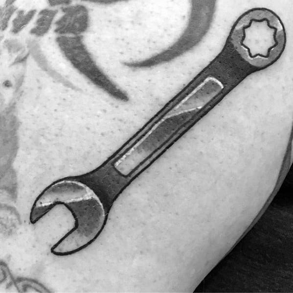Black and grey tattoo of a detailed combination wrench on the upper arm, featuring a star-shaped socket and bold shading.