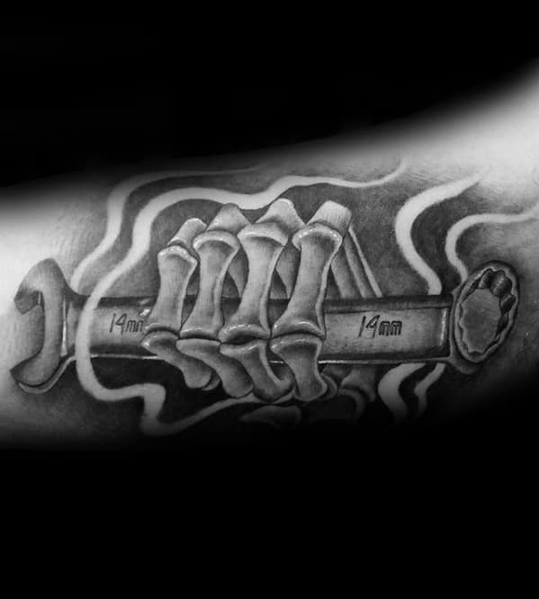 Black and grey tattoo of a skeletal hand gripping a 14mm wrench, surrounded by smoke-like swirls for a bold, eerie effect.